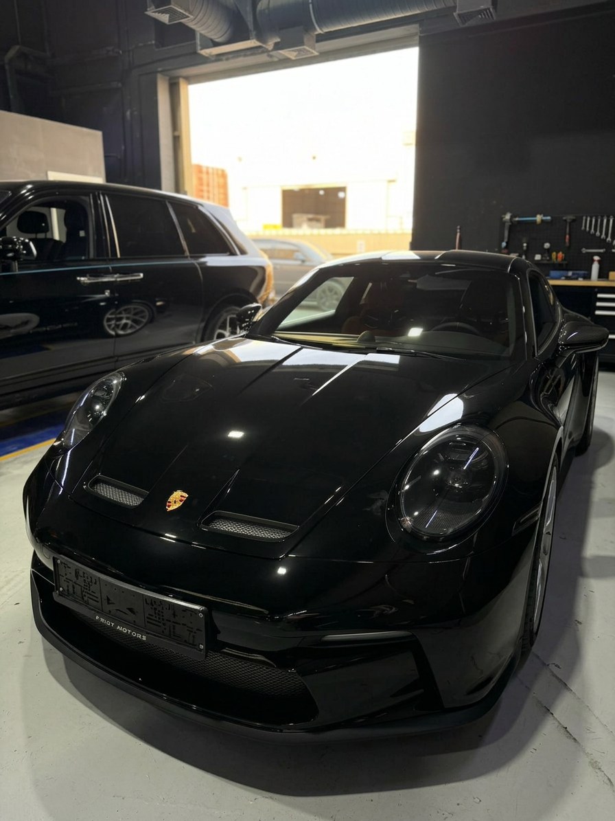 Black Porsche 911 GT3 receiving front-end attention with a Rolls-Royce Cullinan parked alongside